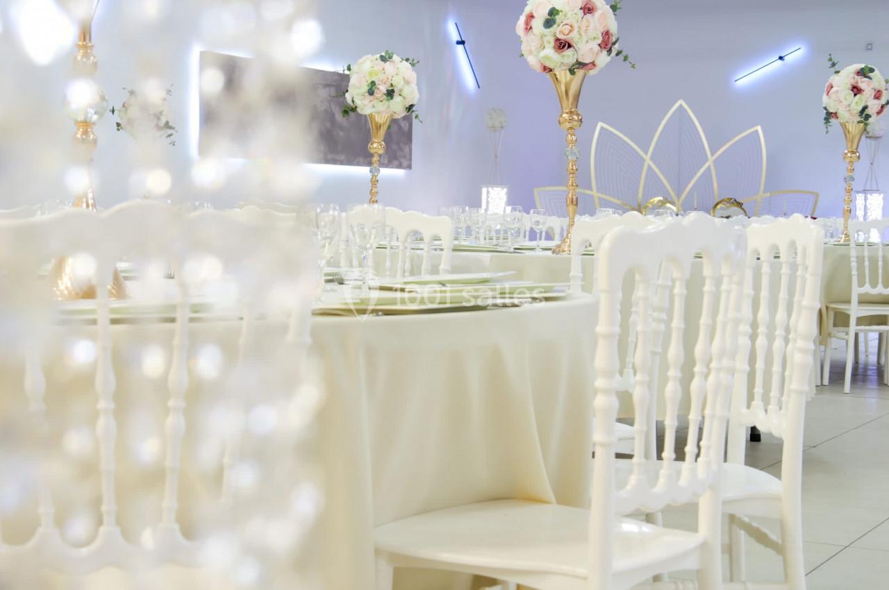 Salle de réception décorée avec des tables rondes, nappes blanches, chaises assorties et centres de table fleuris.