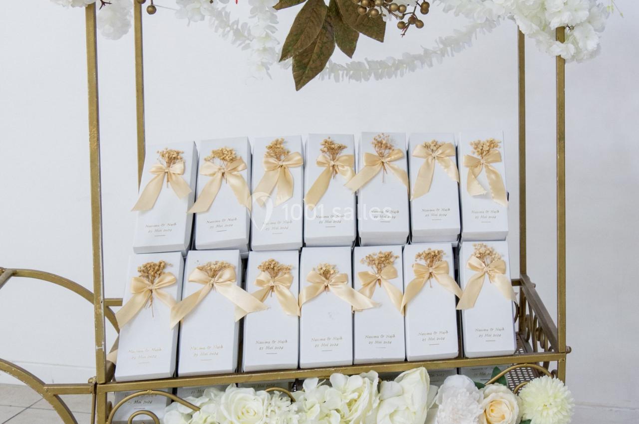 Chariot décoratif en métal doré orné de fleurs blanches, contenant des boîtes blanches avec rubans dorés.