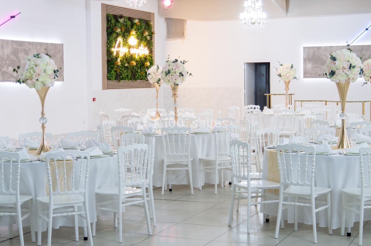 Salle de réception lumineuse avec tables rondes décorées de nappes blanches et centres de table fleuris.