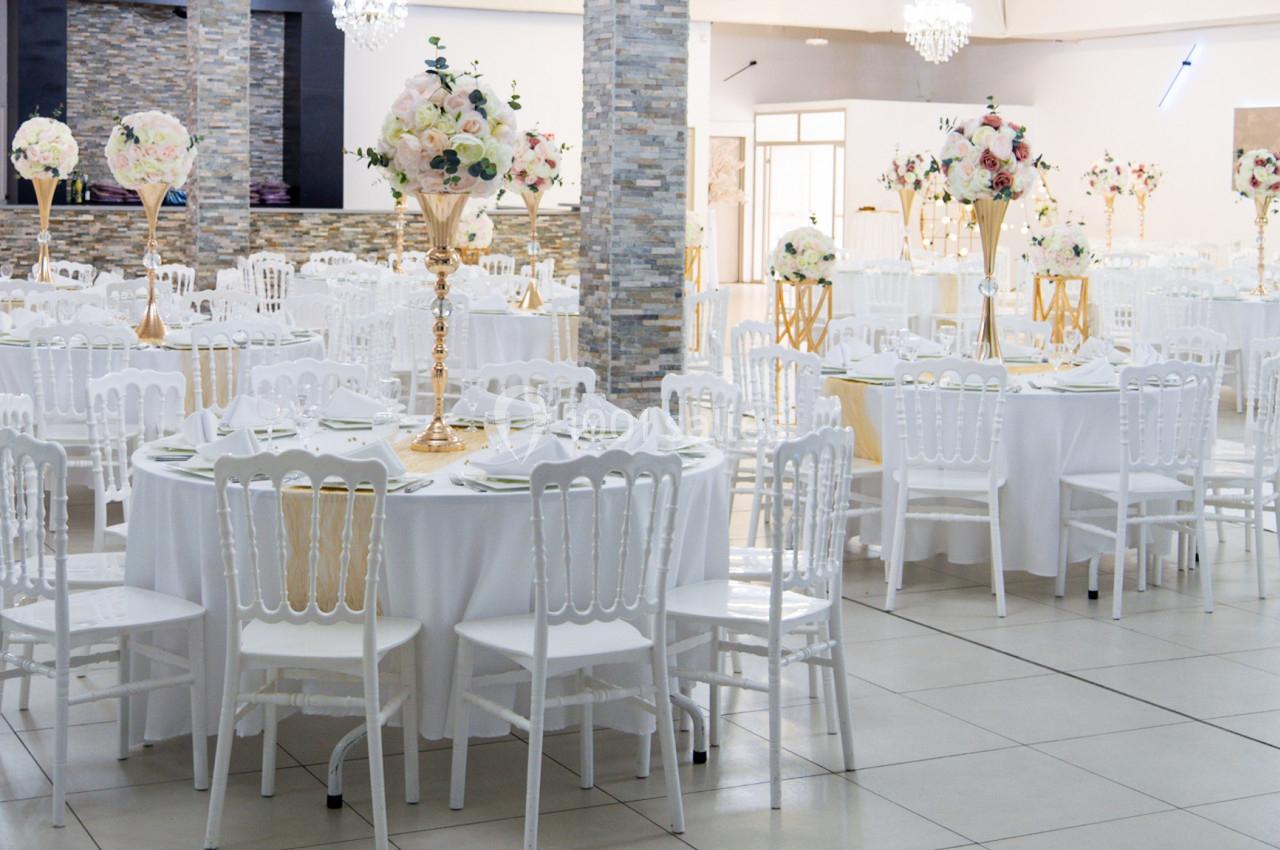 Salle de réception élégante avec tables rondes décorées de centres de table fleuris et chaises blanches.