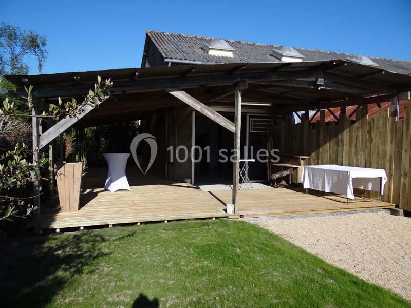 Terrasse en bois couverte attenante à un bâtiment, avec tables dressées et vue sur un jardin.
