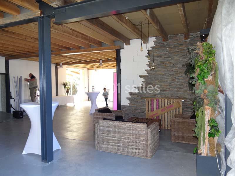 Espace intérieur avec murs en pierre, plafond en bois, mobilier en rotin et tables hautes blanches.