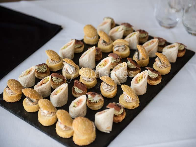 Plateau de canapés variés comprenant roulés, mini-sandwichs et bouchées sur une table blanche.
