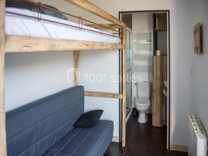 Lit superposé en bois au-dessus d'un canapé, avec vue sur une salle de bain attenante équipée de toilettes.