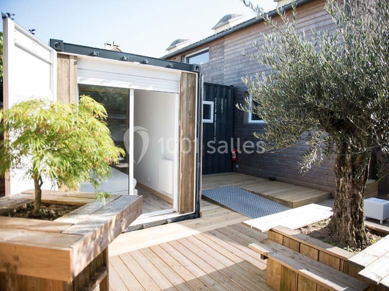 Un conteneur aménagé avec une baie vitrée, entouré de terrasses en bois et de végétation.
