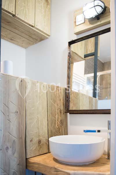 Lavabo rond posé sur un plan en bois, entouré de meubles en bois clair dans une petite salle de bain lumineuse.