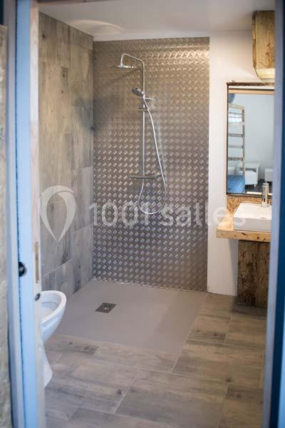 Salle de bain avec douche à l'italienne, carrelage mural texturé, lavabo avec miroir et toilettes.