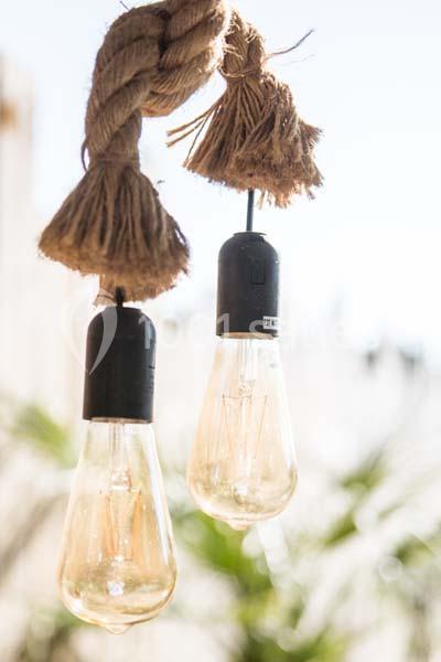 Deux ampoules suspendues à une corde en fibre naturelle, éclairées en plein jour avec un arrière-plan flou.