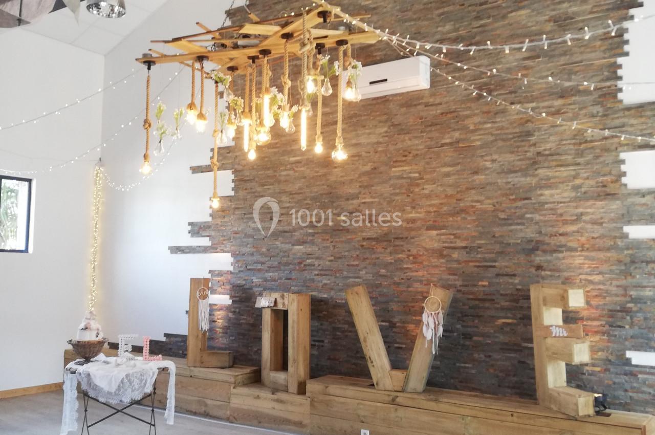 Décoration intérieure avec mur en pierre, guirlandes lumineuses suspendues et éléments en bois dans une salle lumineuse.