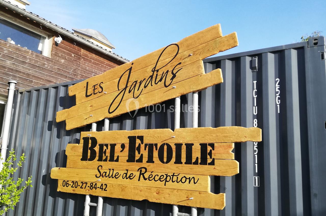 Panneau en bois indiquant ’Les Jardins Bel'Étoile, Salle de Réception’ devant un conteneur gris.