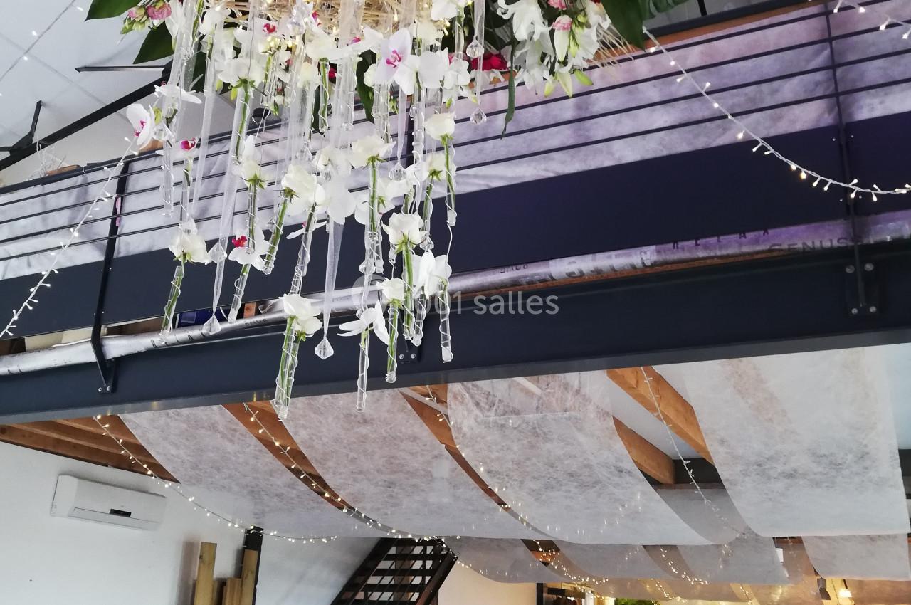 Décoration florale suspendue avec guirlandes lumineuses dans une salle de réception moderne à deux niveaux.