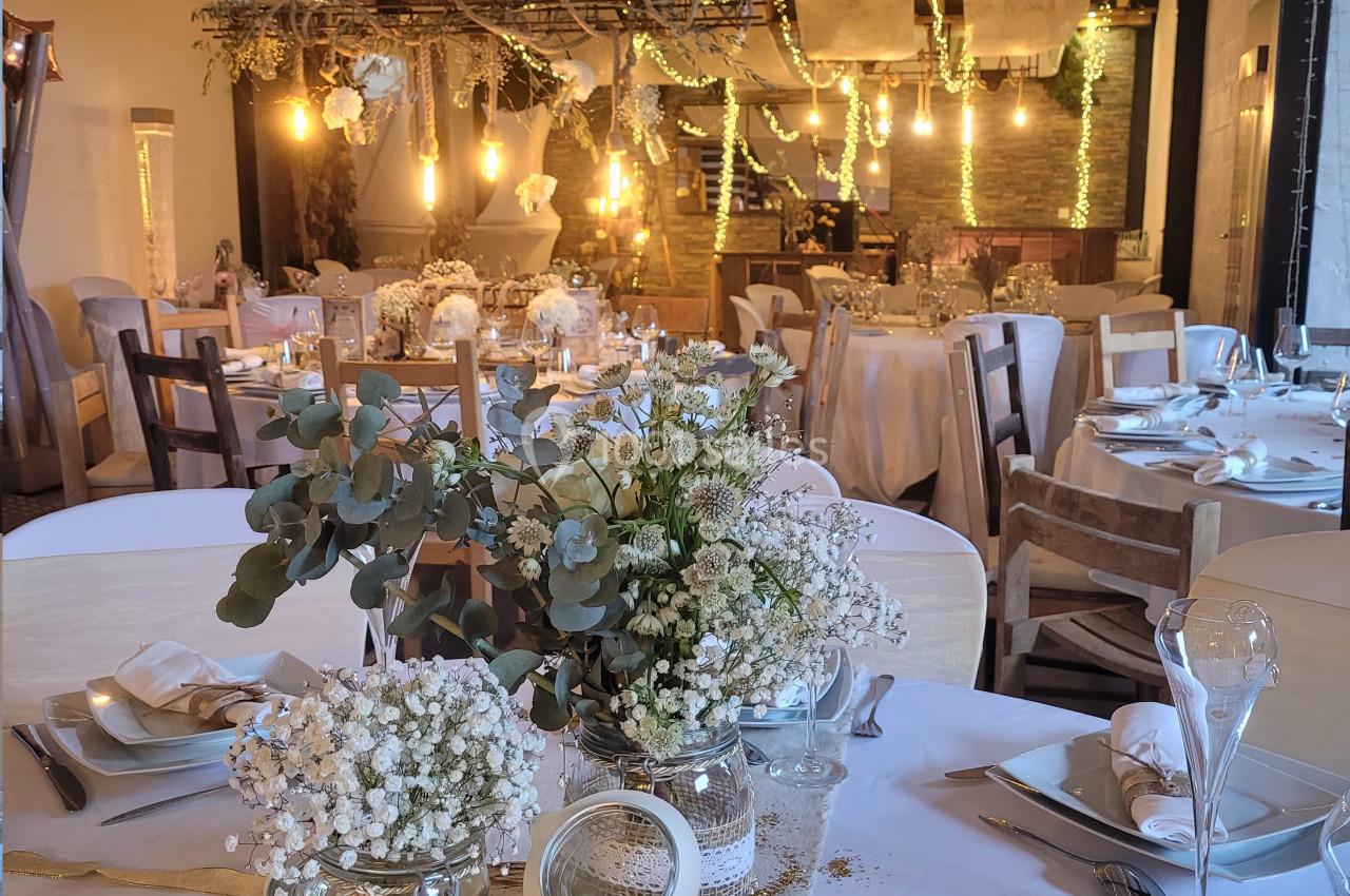 Salle de réception décorée pour un mariage avec tables dressées, guirlandes lumineuses et fleurs blanches.