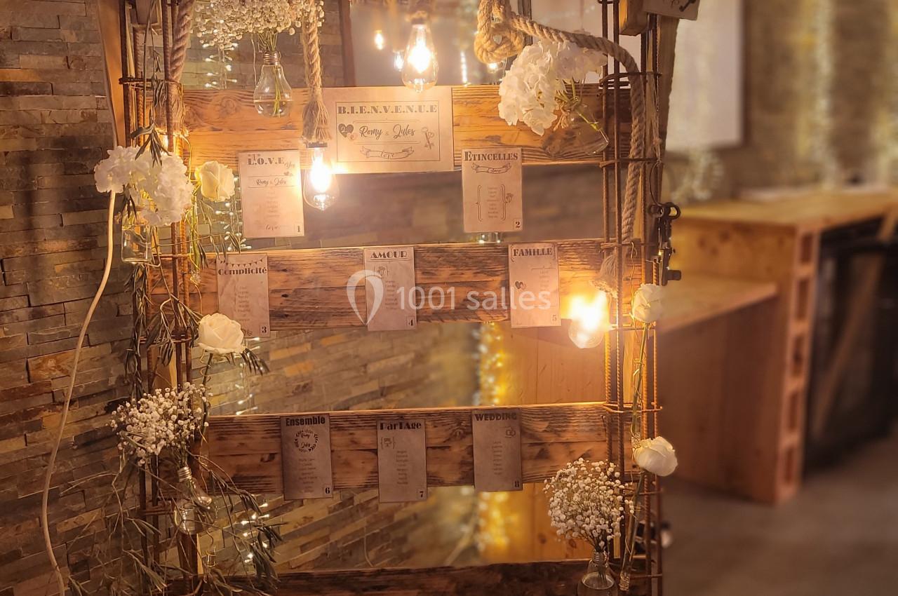 Plan de tables décoratif avec fleurs blanches, guirlandes lumineuses et cartes de placement suspendues sur une structure en…