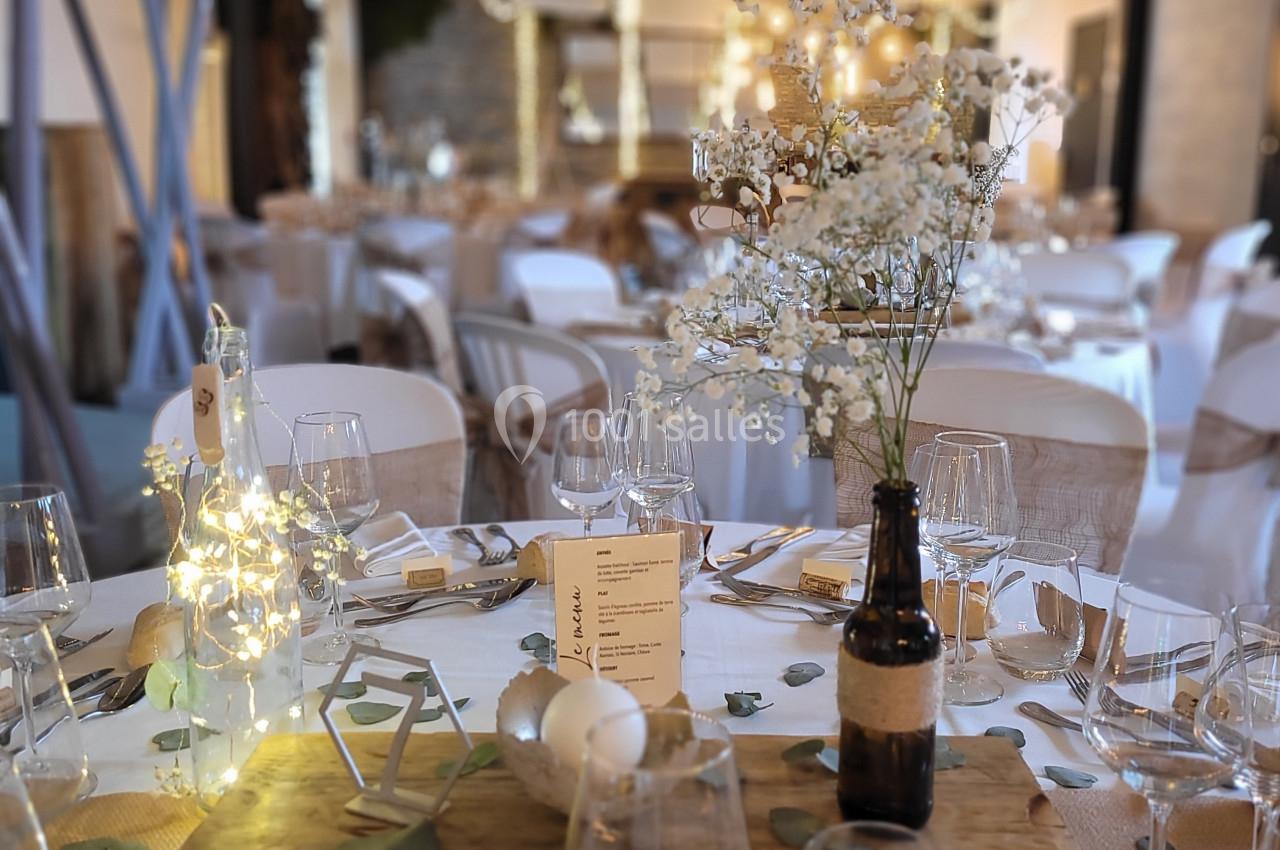 Salle de réception décorée pour un mariage, avec tables dressées, guirlandes lumineuses et centre de table floral.