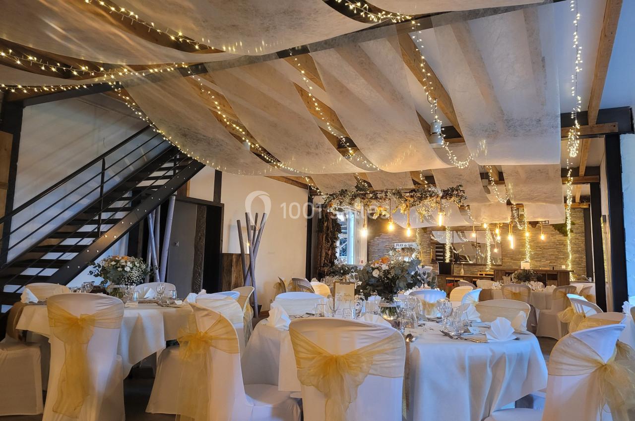Salle de réception décorée avec des guirlandes lumineuses, des tables dressées et des chaises ornées de nœuds jaunes.