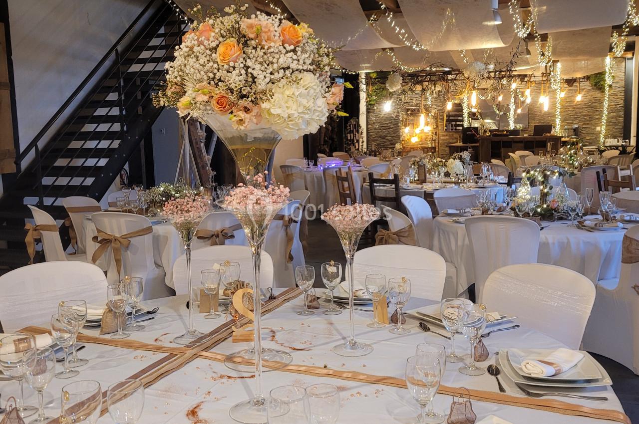 Salle de réception décorée avec des tables rondes élégantes, nappes blanches, fleurs et guirlandes lumineuses suspendues.
