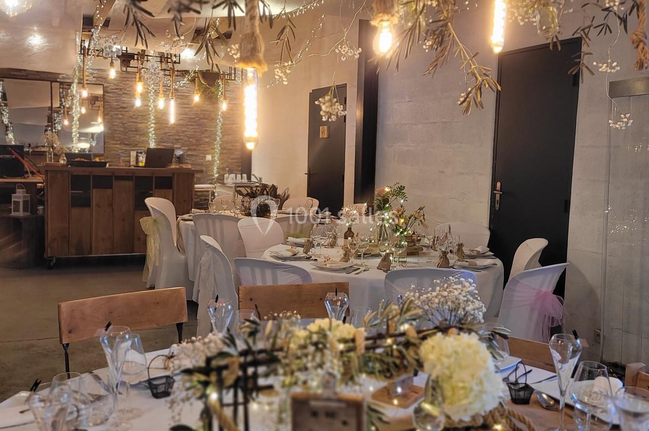 Salle de réception décorée avec des tables dressées, guirlandes lumineuses et ornements floraux suspendus.