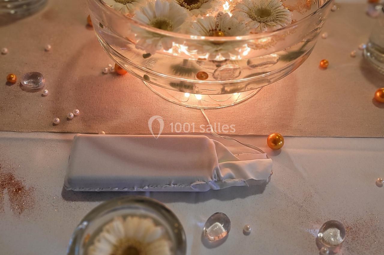 Bol en verre contenant des fleurs blanches flottantes, entouré de perles et décorations sur une table élégante.