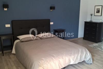 Chambre avec un lit double, tête de lit noire, tables de chevet, mur bleu et mobilier sombre sur un sol en parquet clair.