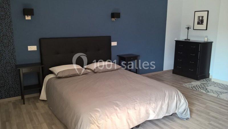 Chambre avec un lit double, tête de lit noire, tables de chevet, mur bleu et mobilier sombre sur un sol en parquet clair.