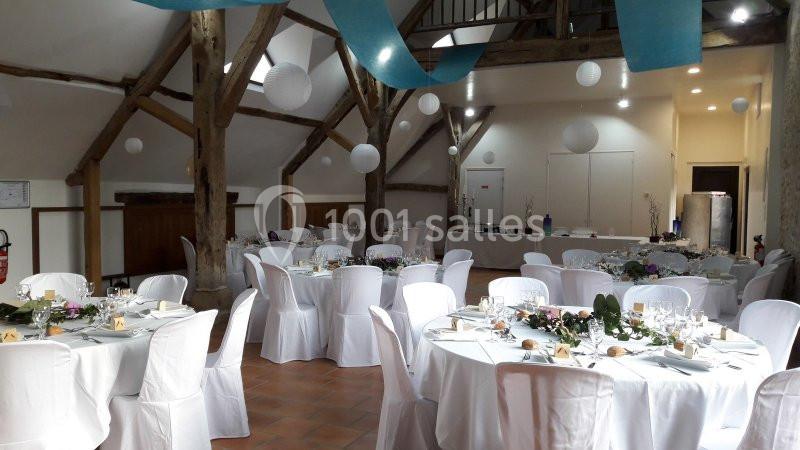 Salle de réception décorée avec des tables rondes dressées, nappes blanches, guirlandes et lanternes suspendues.