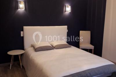 Chambre avec un lit double, tête de lit noire, tables de chevet, mur bleu et mobilier sombre sur un sol en parquet clair.