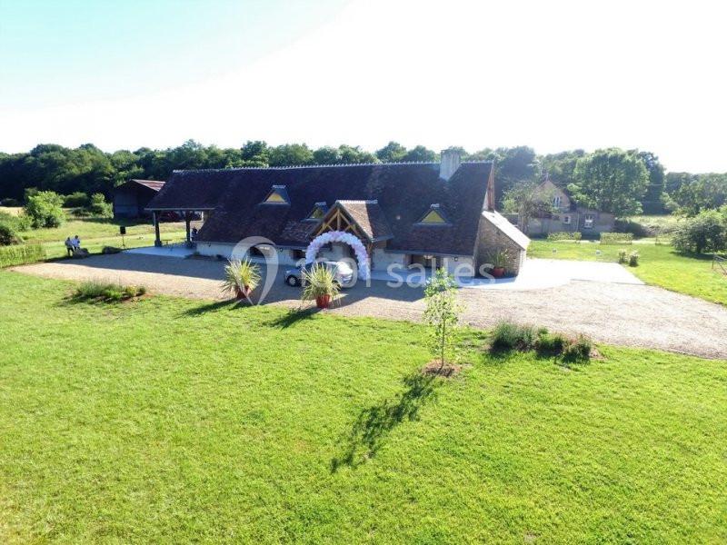 Vue aérienne d'une maison traditionnelle avec toit en tuiles, entourée de pelouses et d'arbres dans un cadre rural.