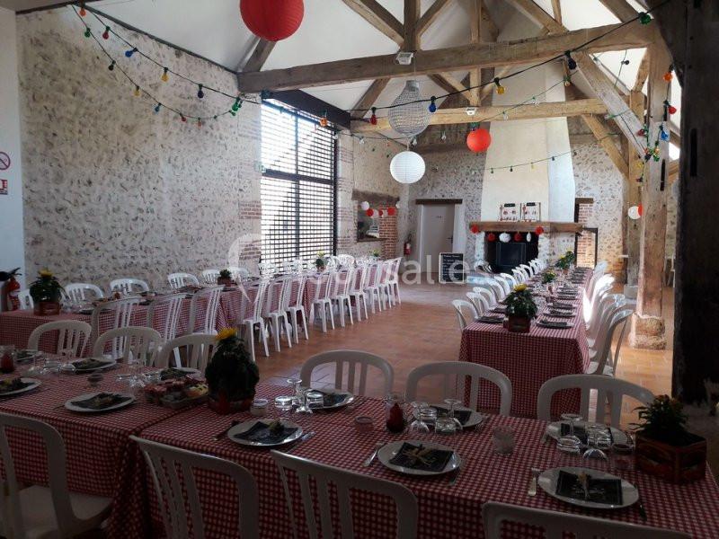 Salle décorée pour un repas festif avec tables alignées, nappes à carreaux rouges, guirlandes lumineuses et lanternes…