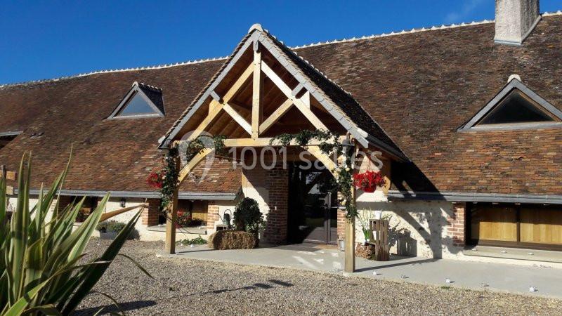 Entrée d'une bâtisse traditionnelle avec toit en tuiles, charpente en bois et décoration florale.