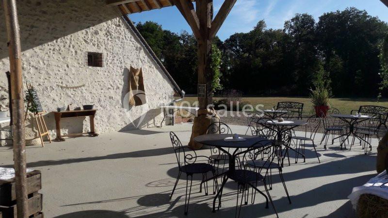 Terrasse extérieure avec tables et chaises en fer forgé, adossée à un bâtiment en pierre sous un ciel dégagé.