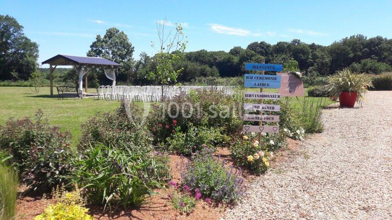Jardin avec fleurs, allée gravillonnée, panneau directionnel coloré et espace aménagé pour une cérémonie en plein air.