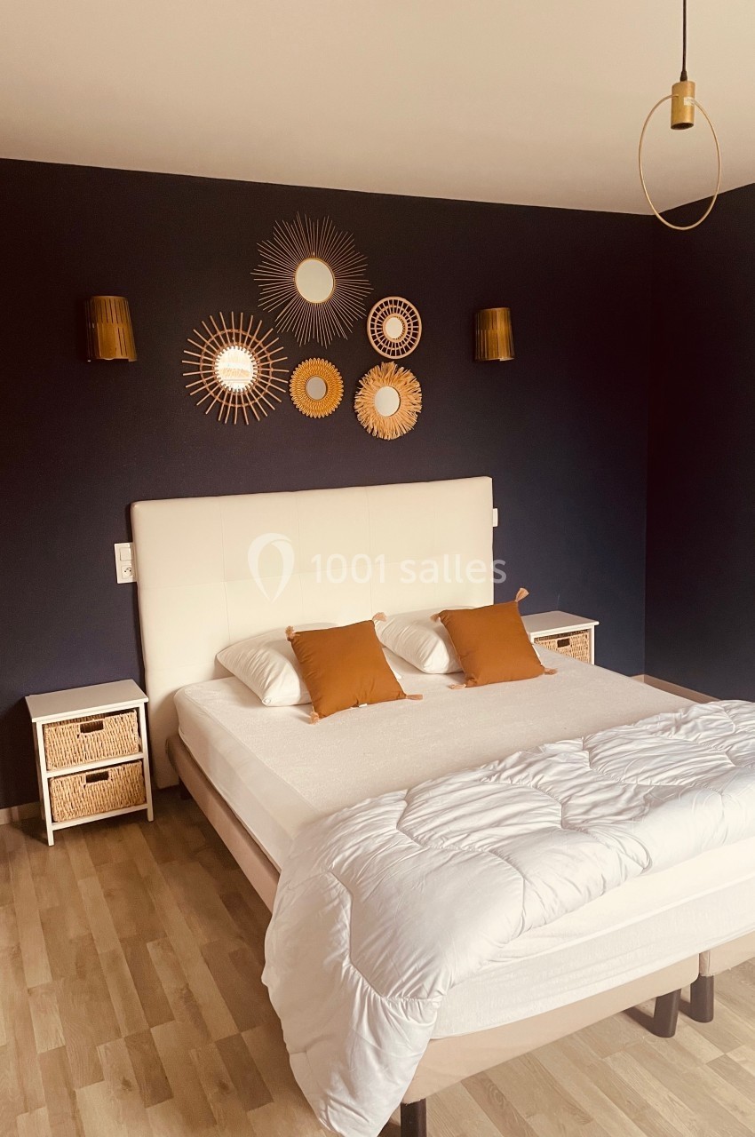 Chambre avec lit double, mur bleu décoré de miroirs dorés, tables de chevet en rotin et luminaires assortis.