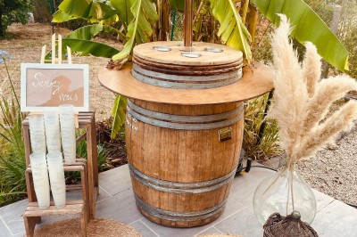 Tonneau en bois transformé en bar avec décoration végétale, verres et pancarte ’Servez-vous’ dans un jardin.