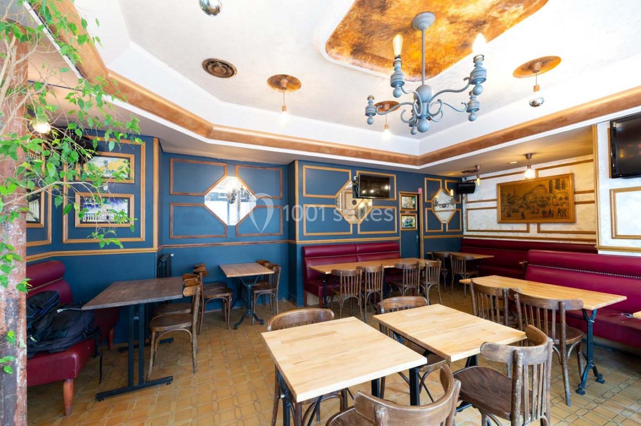 Salle de restaurant vide avec tables en bois, chaises, banquettes rouges, murs décorés et un lustre central.