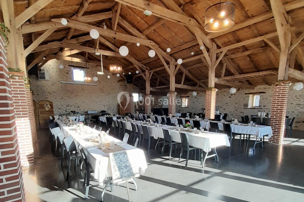 Salle de réception lumineuse avec charpente en bois, tables dressées et décoration suspendue.