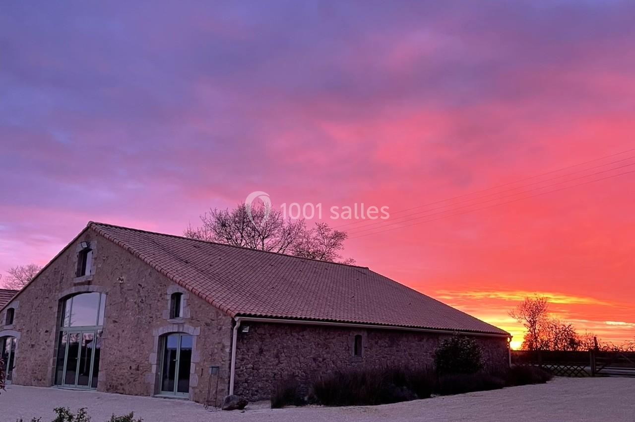 Bâtiment en pierre avec toit en tuiles, éclairé par un coucher de soleil aux teintes roses et violettes.