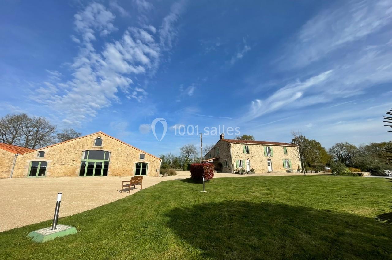 Deux bâtiments en pierre avec des toits rouges entourés de pelouses et d'arbres sous un ciel partiellement nuageux.