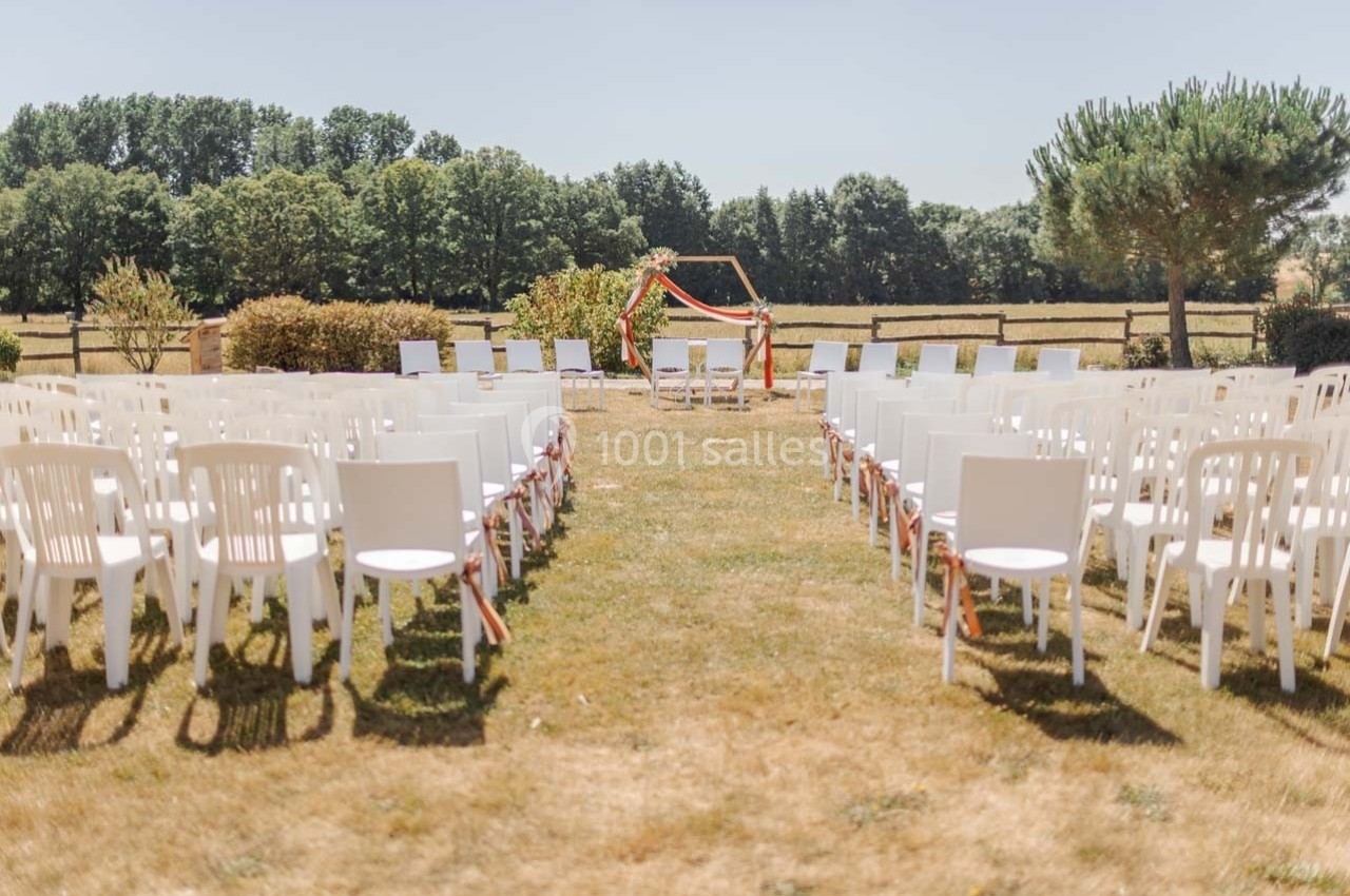 Chaises blanches alignées en extérieur face à une arche décorée pour une cérémonie dans un cadre champêtre.