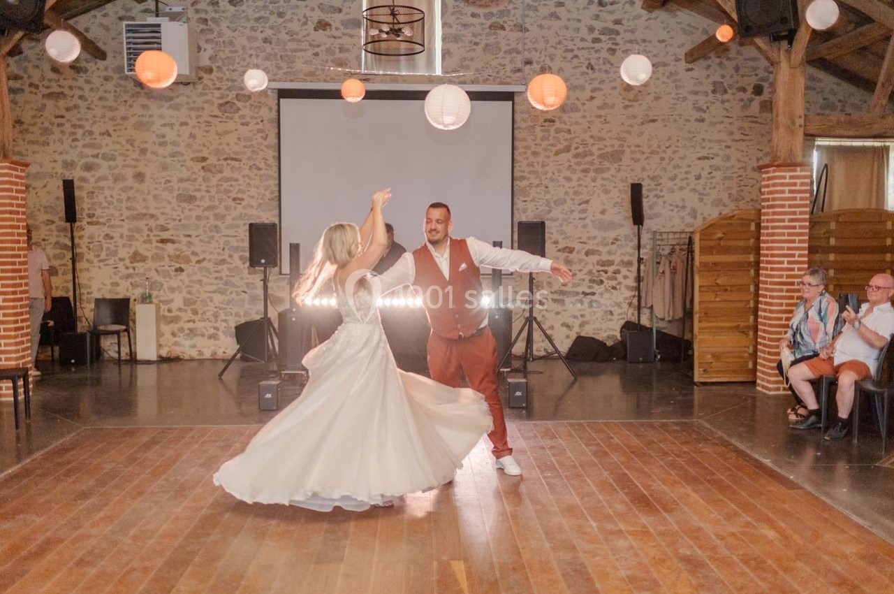 Un couple danse dans une salle en pierre décorée de lanternes suspendues, sous le regard de quelques spectateurs assis.
