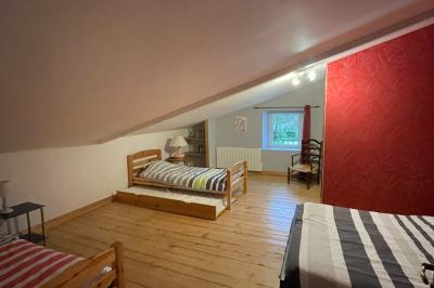 Chambre avec lits superposés en bois, parquet, papier peint floral, accès à une salle de bain et vue sur un jardin.
