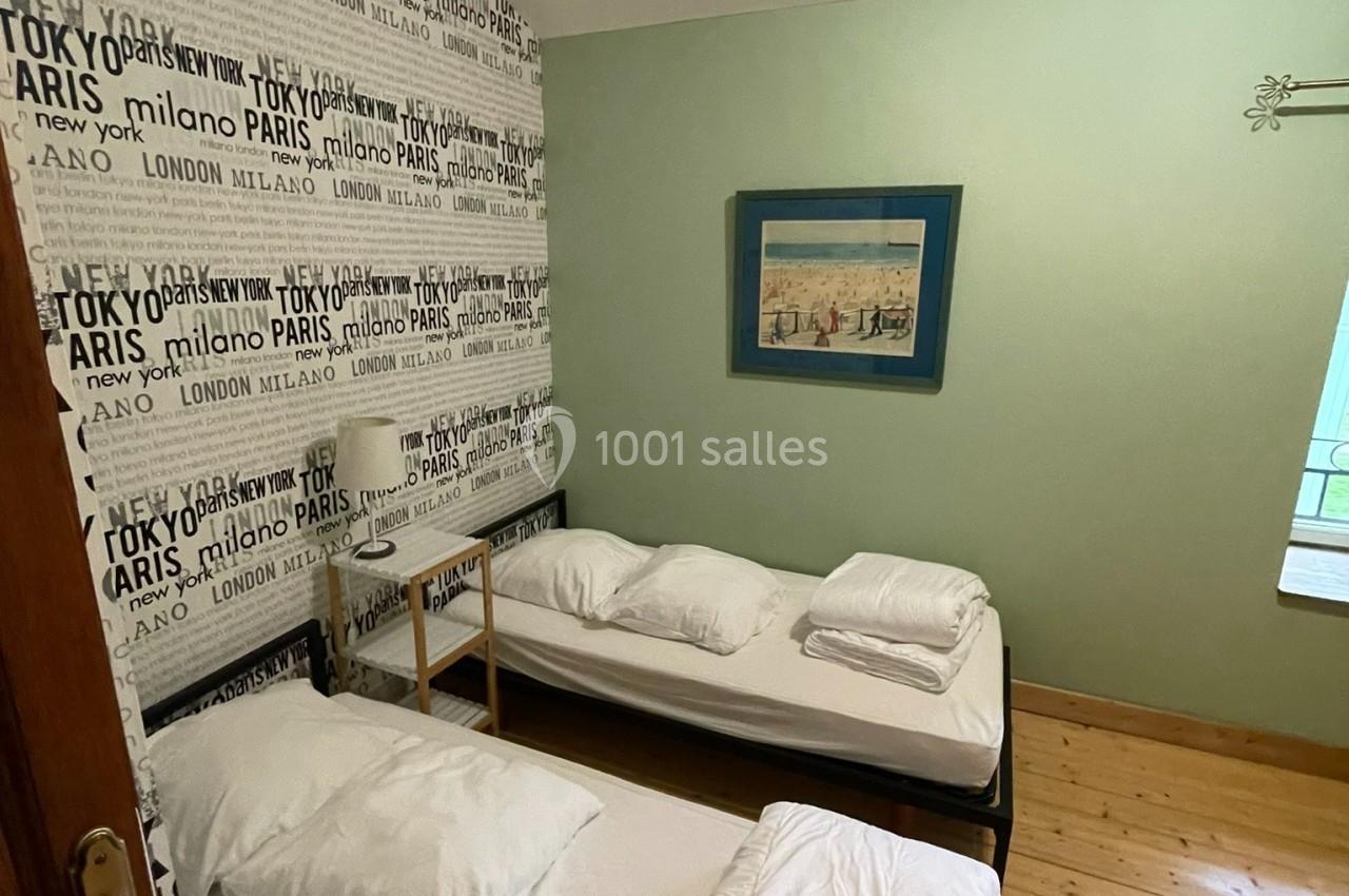 Deux lits simples avec draps blancs dans une chambre au sol en bois, décorée d'un mur avec des noms de villes.