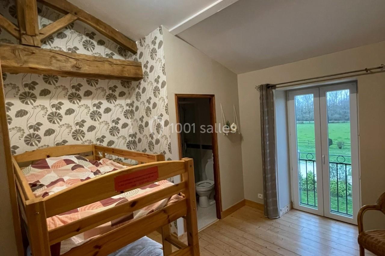 Chambre avec lits superposés en bois, parquet, papier peint floral, accès à une salle de bain et vue sur un jardin.