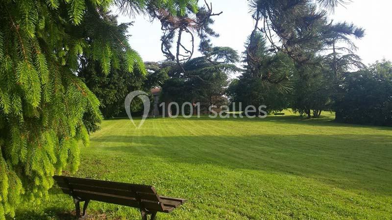 Banc en bois face à une pelouse verdoyante entourée d'arbres dans un parc sous un ciel dégagé.