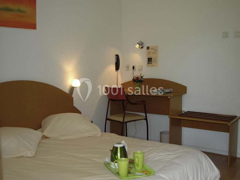 Chambre avec lit double, bureau en bois, chaise, lampe murale, plateau avec théière et tasses sur le lit.