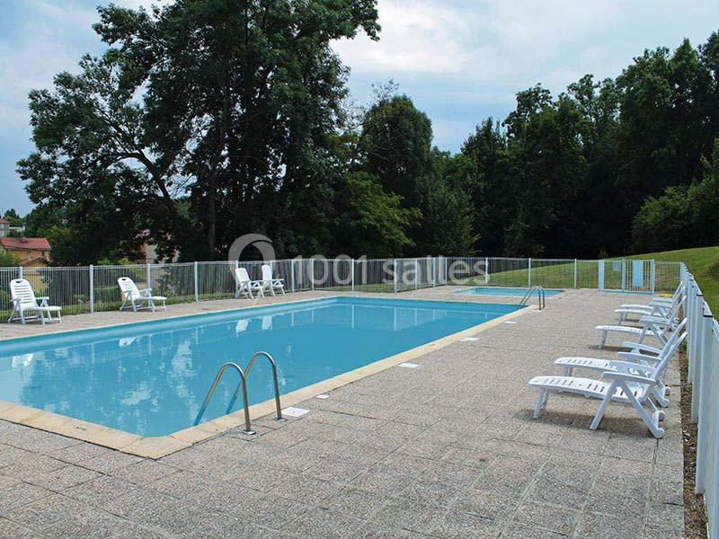 Piscine extérieure entourée de chaises longues blanches, avec des arbres en arrière-plan.