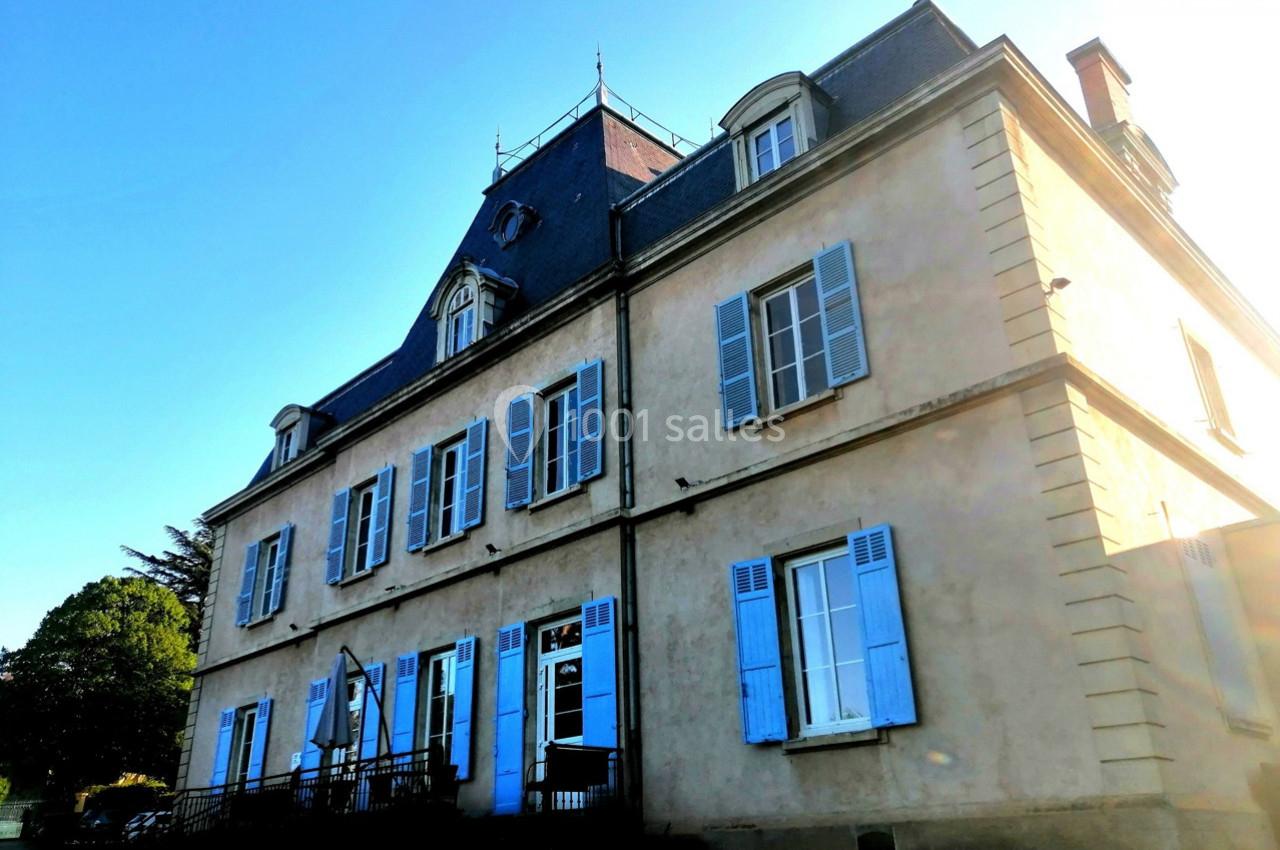 Façade d'une grande maison ancienne avec des volets bleus, un toit en ardoise et un ciel dégagé en arrière-plan.