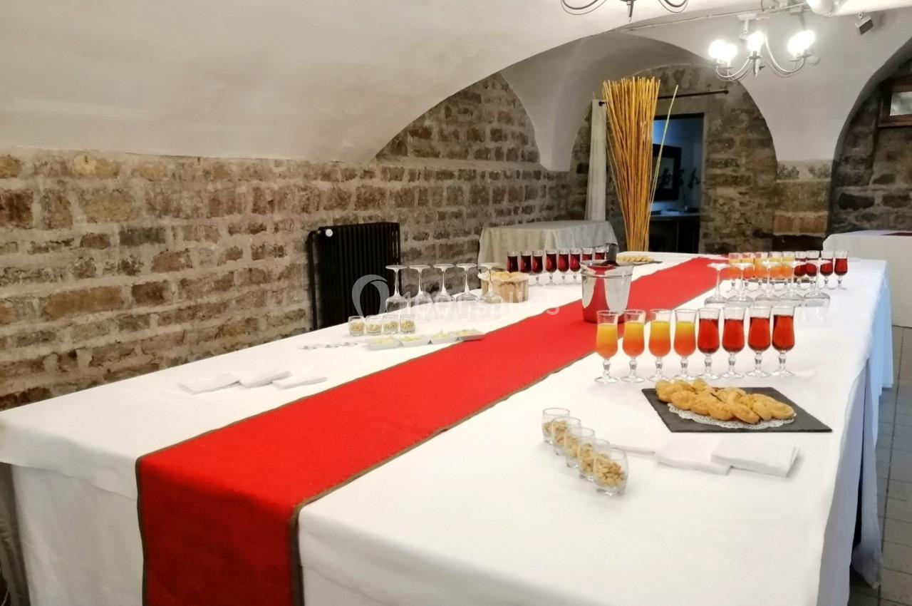 Table dressée avec une nappe blanche et un chemin de table rouge, garnie de verres, amuse-bouches et décorations.