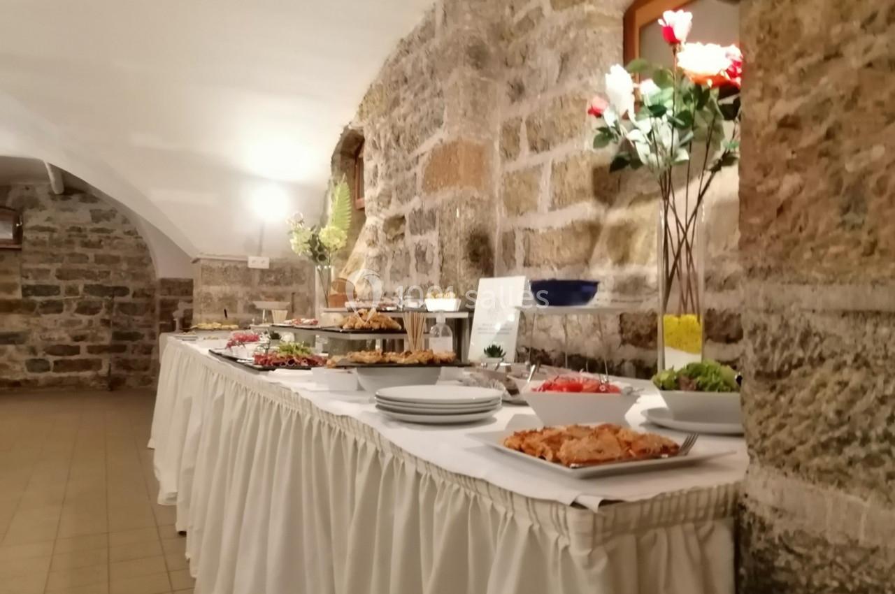 Buffet varié disposé sur une table drapée dans une salle en pierre avec éclairage chaleureux et décor floral.