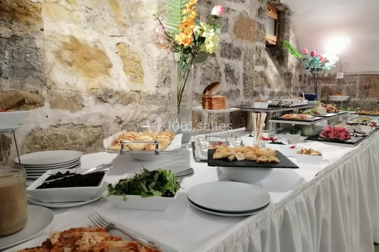 Buffet varié avec plats salés, salades, pains et décorations florales, disposé sur une table blanche dans une salle en…
