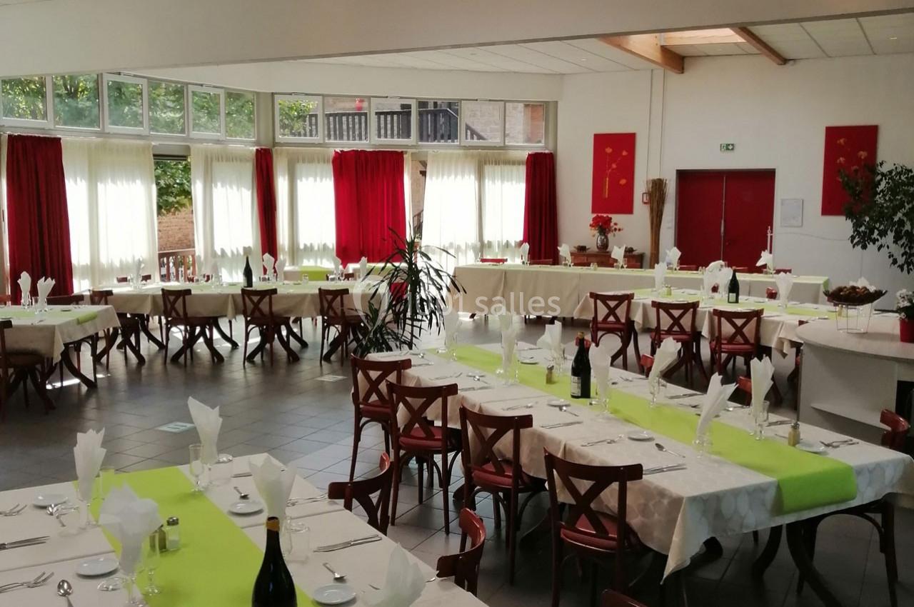 Salle de réception lumineuse avec tables dressées, nappes blanches et chemins de table verts, prête pour un événement.